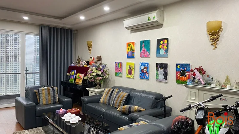 Phòng khách trước cải tạo, với sofa tối màu, đàn piano và nền gỗ.